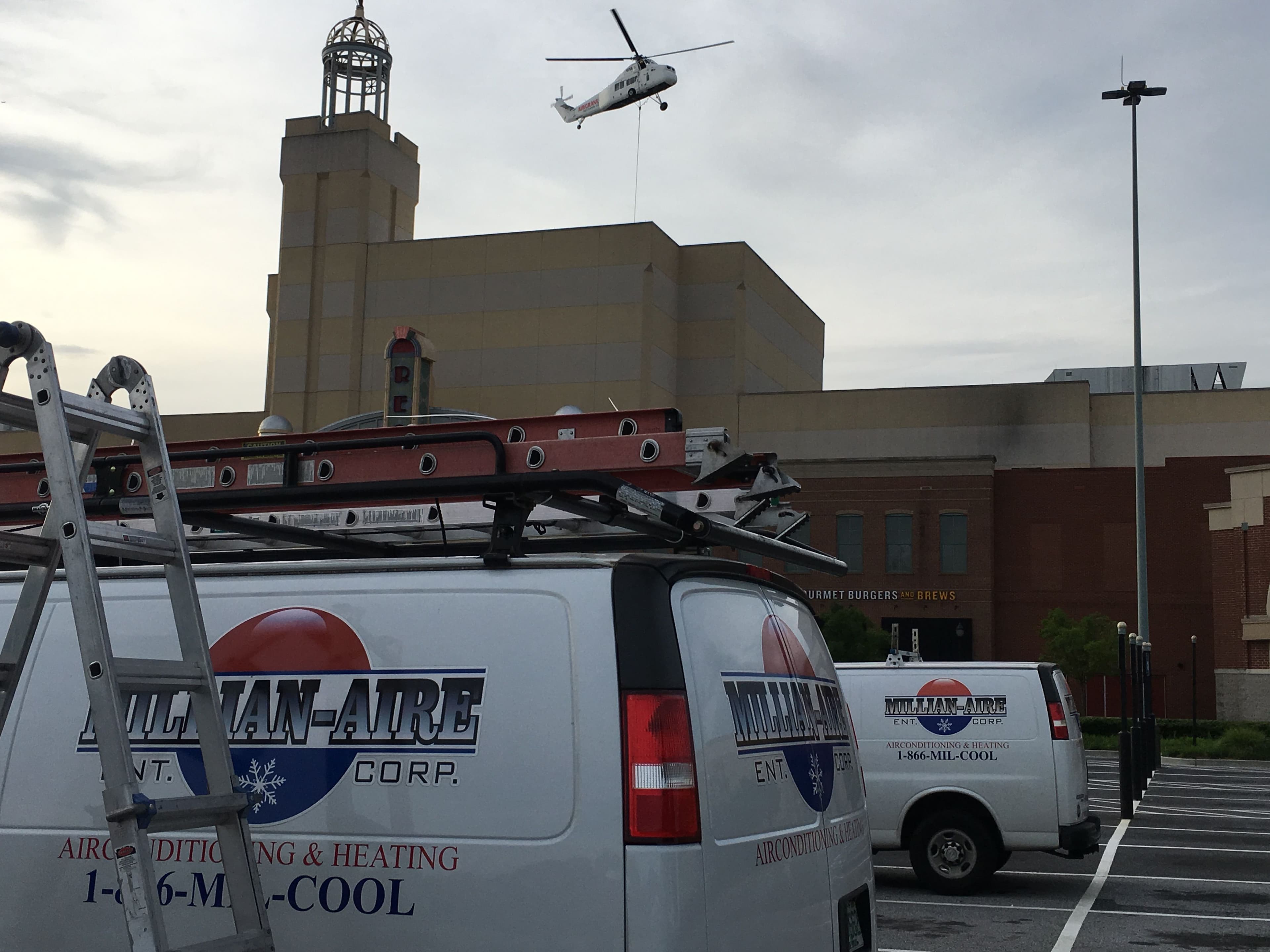 Millian Aire HVAC van on-site at the Mall of Georgia with a helicopter lifting rooftop HVAC units in the background during a commercial installation for Regal Cinemas.
